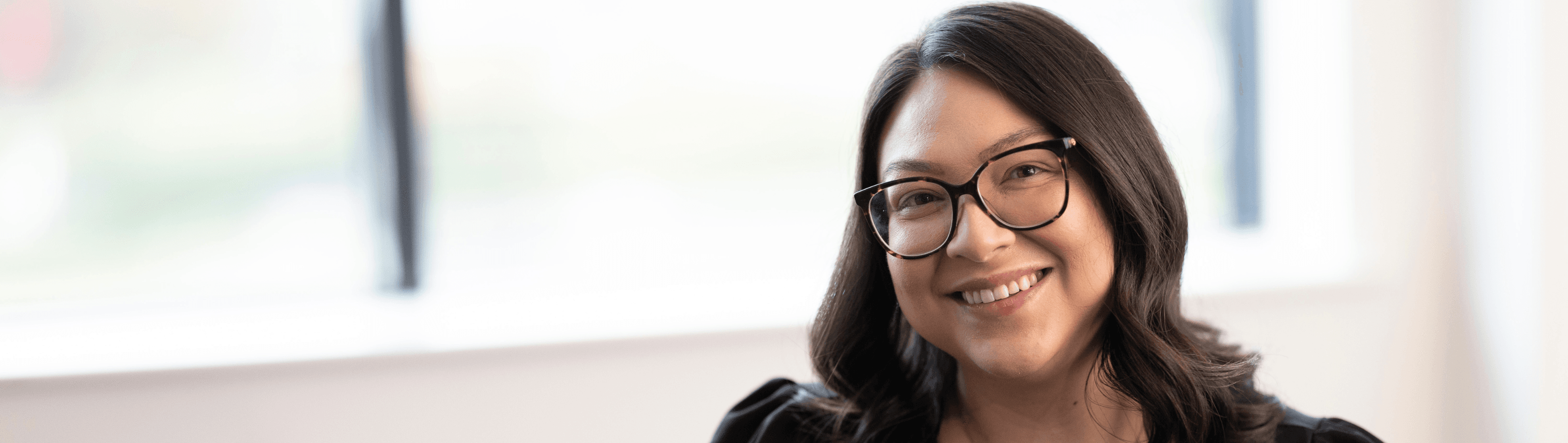 A woman with dark hair and glasses, smiling, indoors