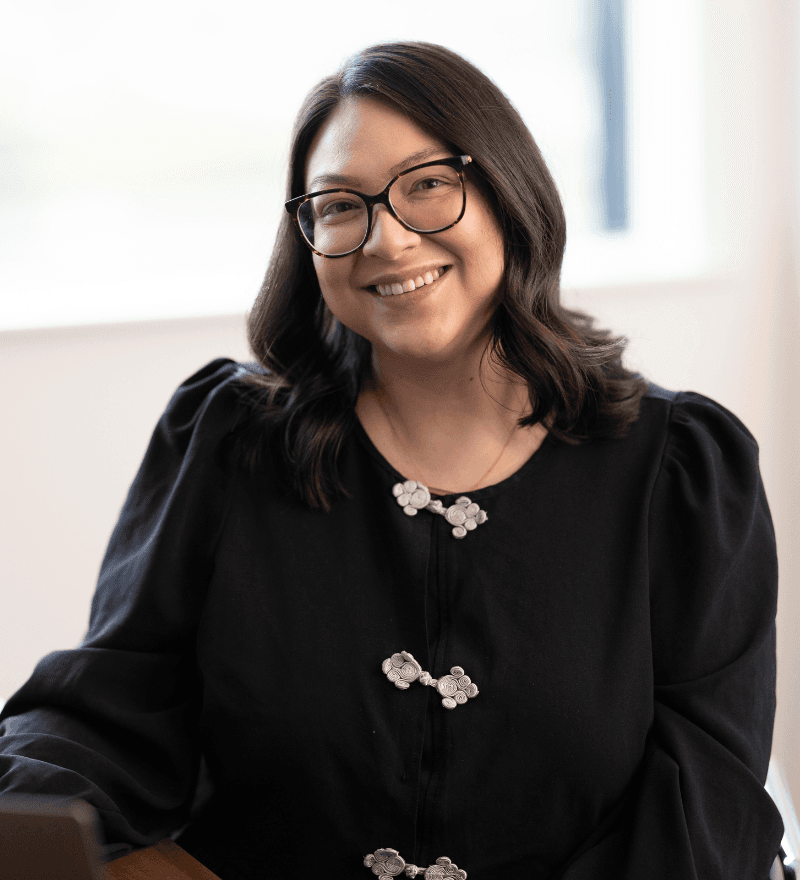 A woman with dark hair and glasses, smiling, indoors