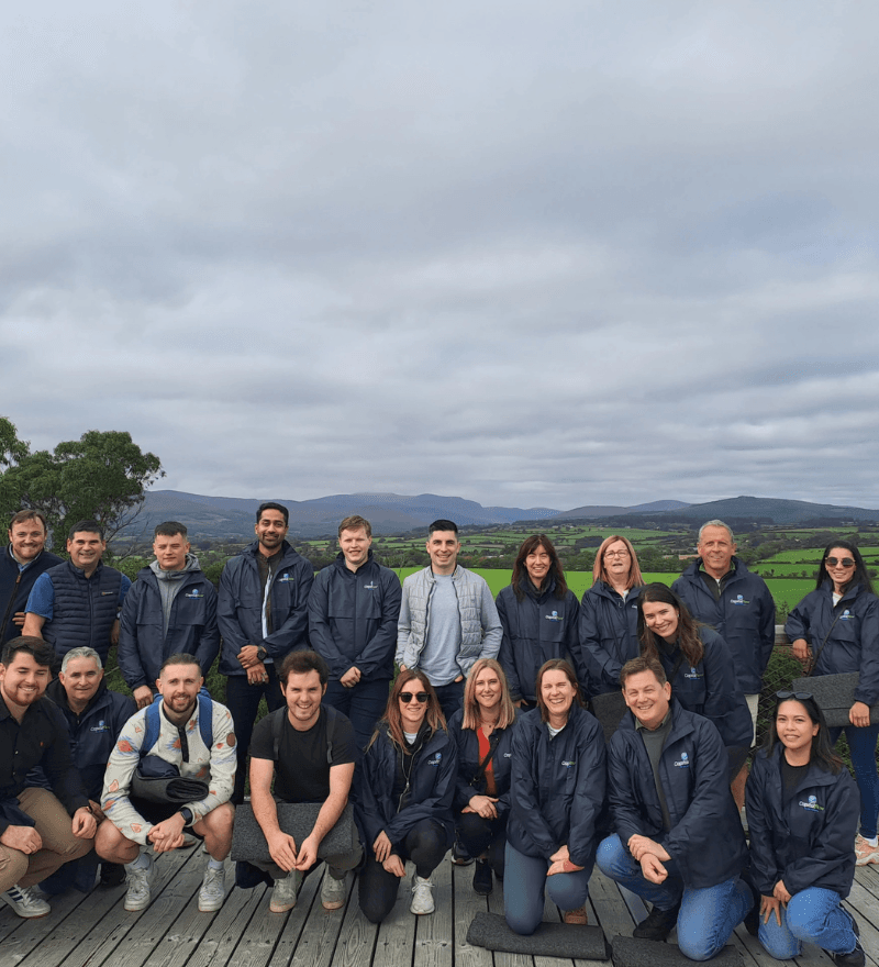 A group standing outdoors on a hillside with mountains and fields in the background