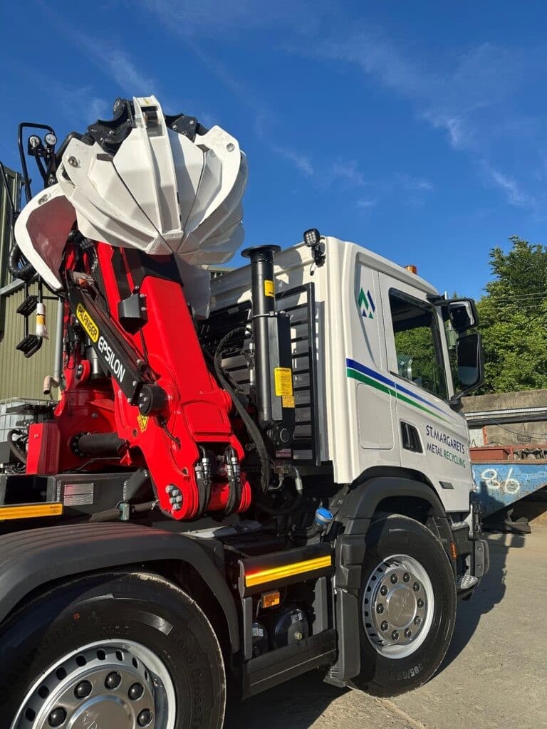 Close-up of a red and white waste collection truck with mechanical arm outdoors