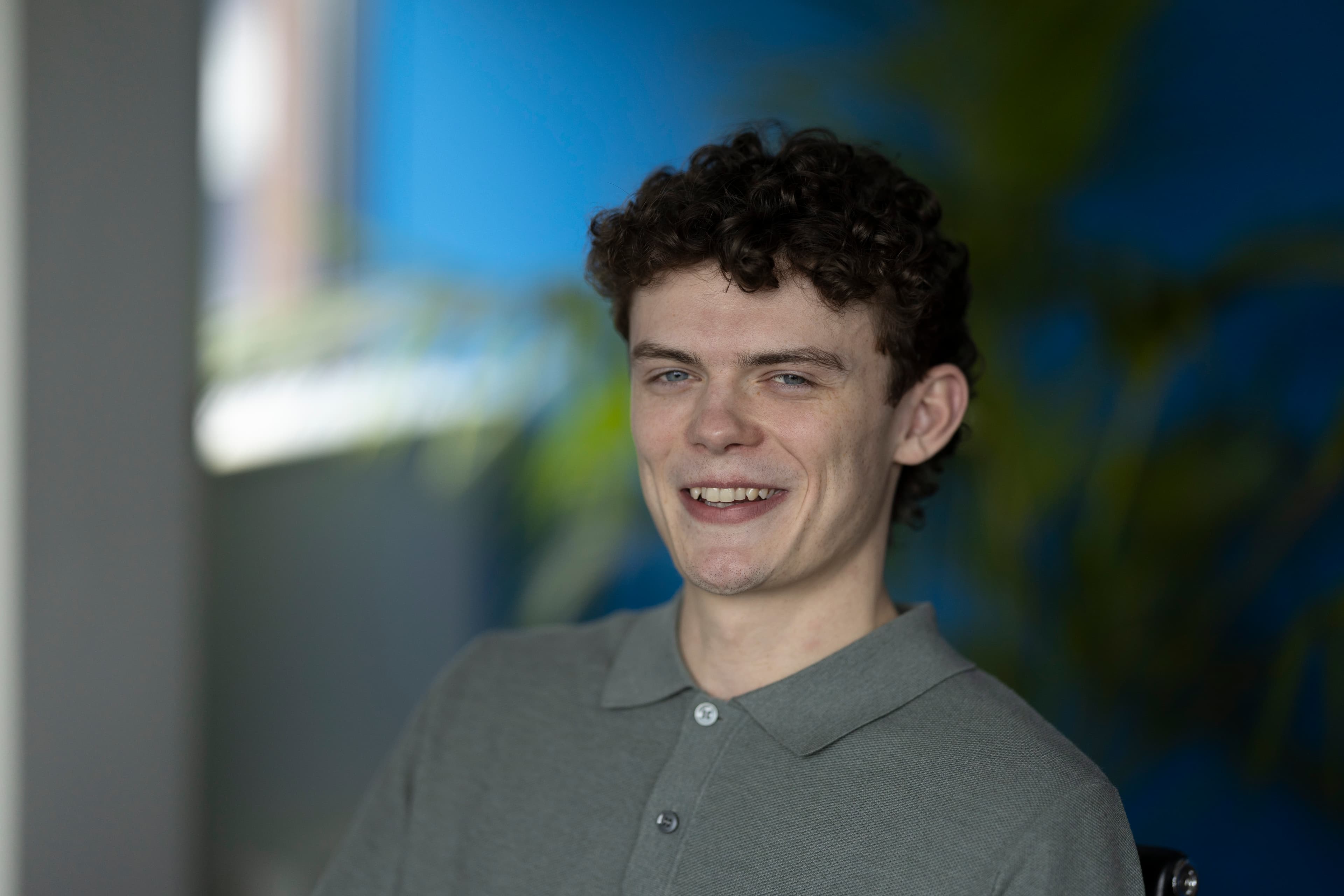 Tom R — young man with curly dark hair, smiling, blue background