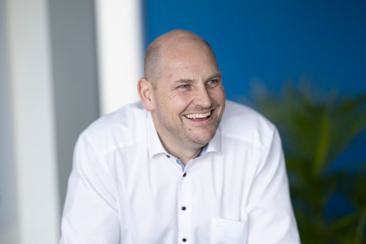 Bald man in white shirt, broad smile, blue office background