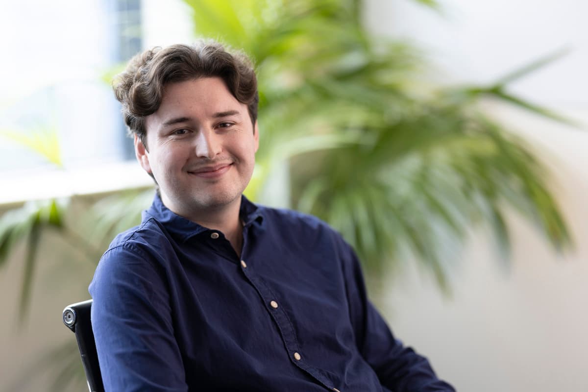 Thomas Freeman — man with curly dark hair, blue shirt, smiling, plant background