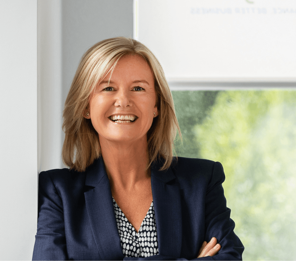 Woman with blonde hair, dark blazer, smiling outdoors in bright light