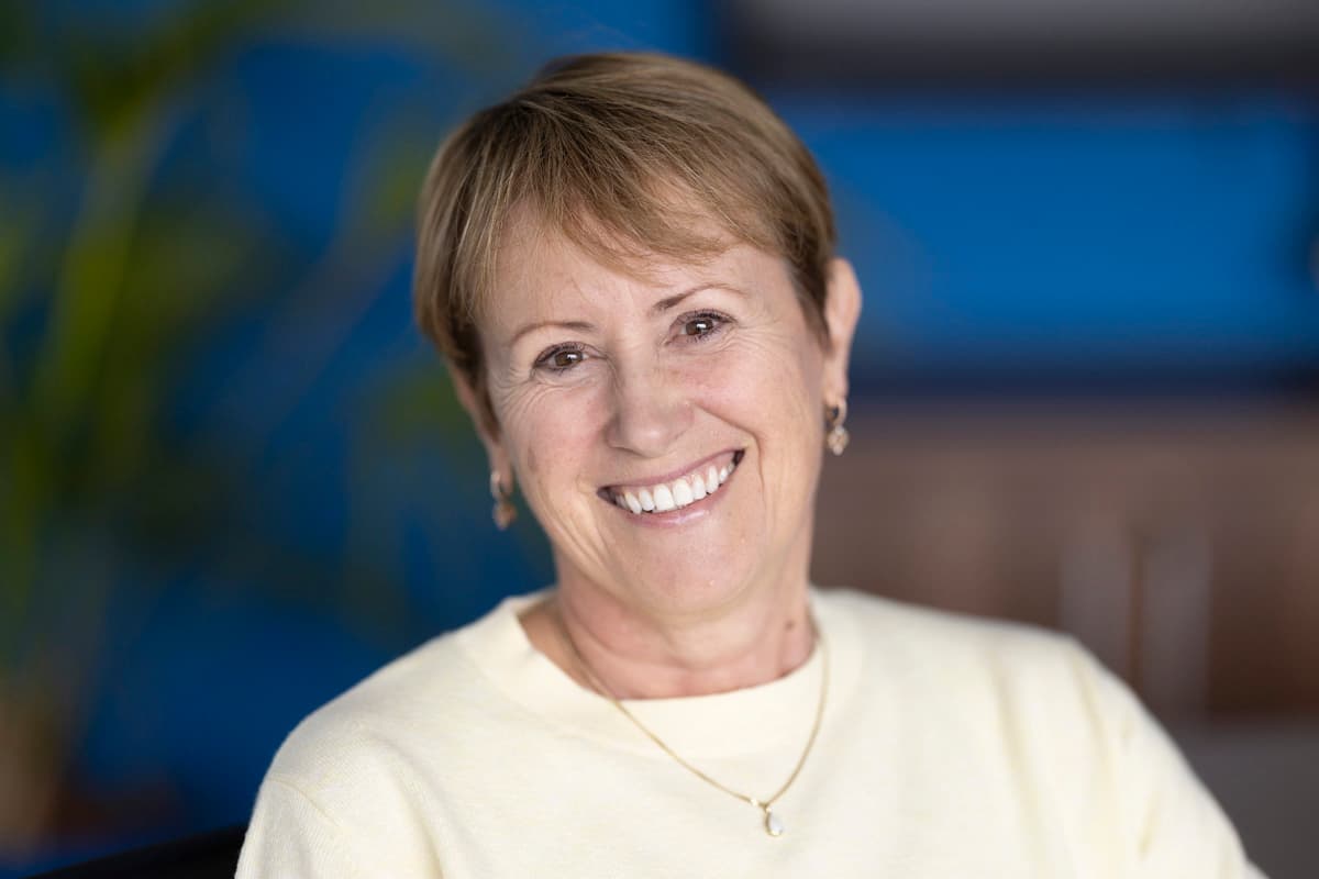 Headshot of a smiling woman with grey-blonde hair, plain background