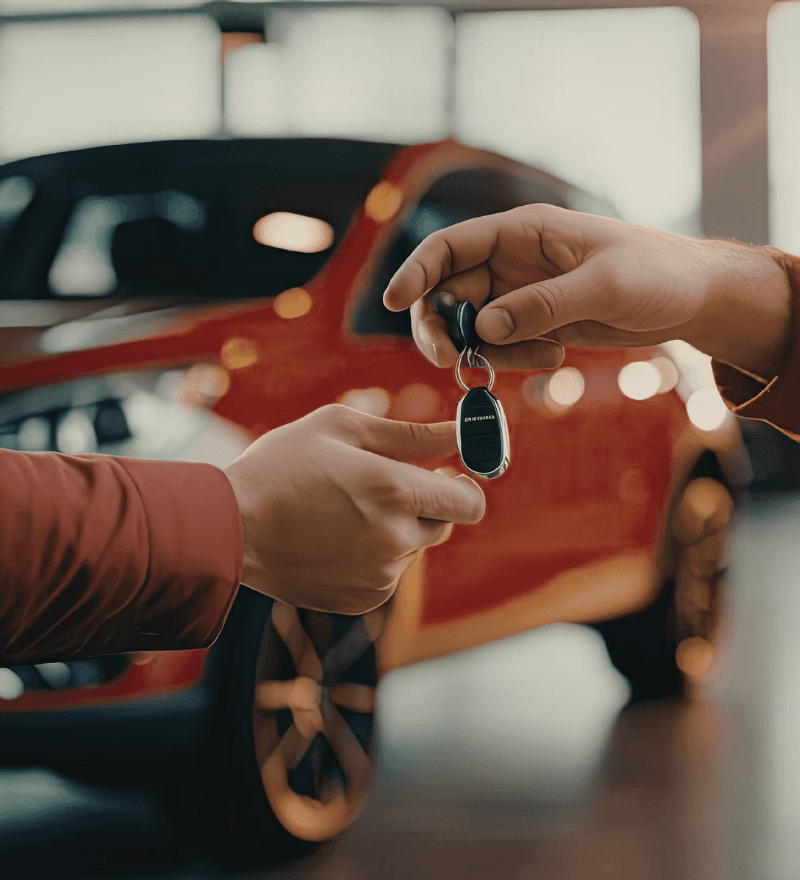 A close-up of hands exchanging car keys over a red car