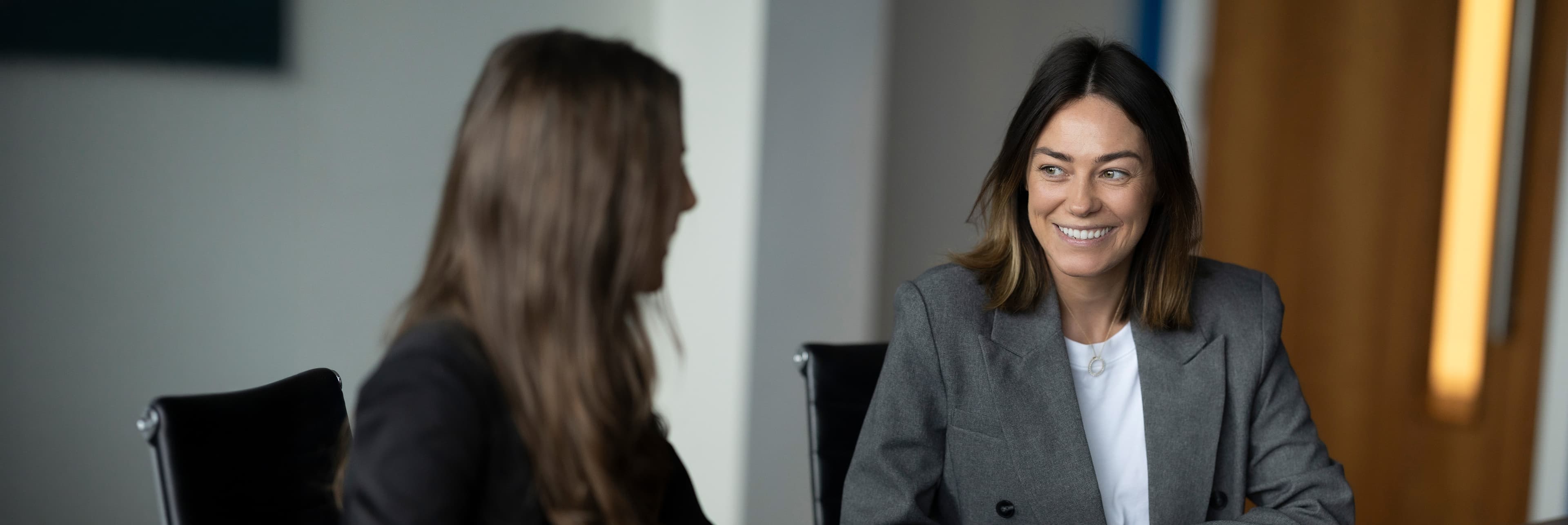 Two women in conversation, one seated, blurred office setting