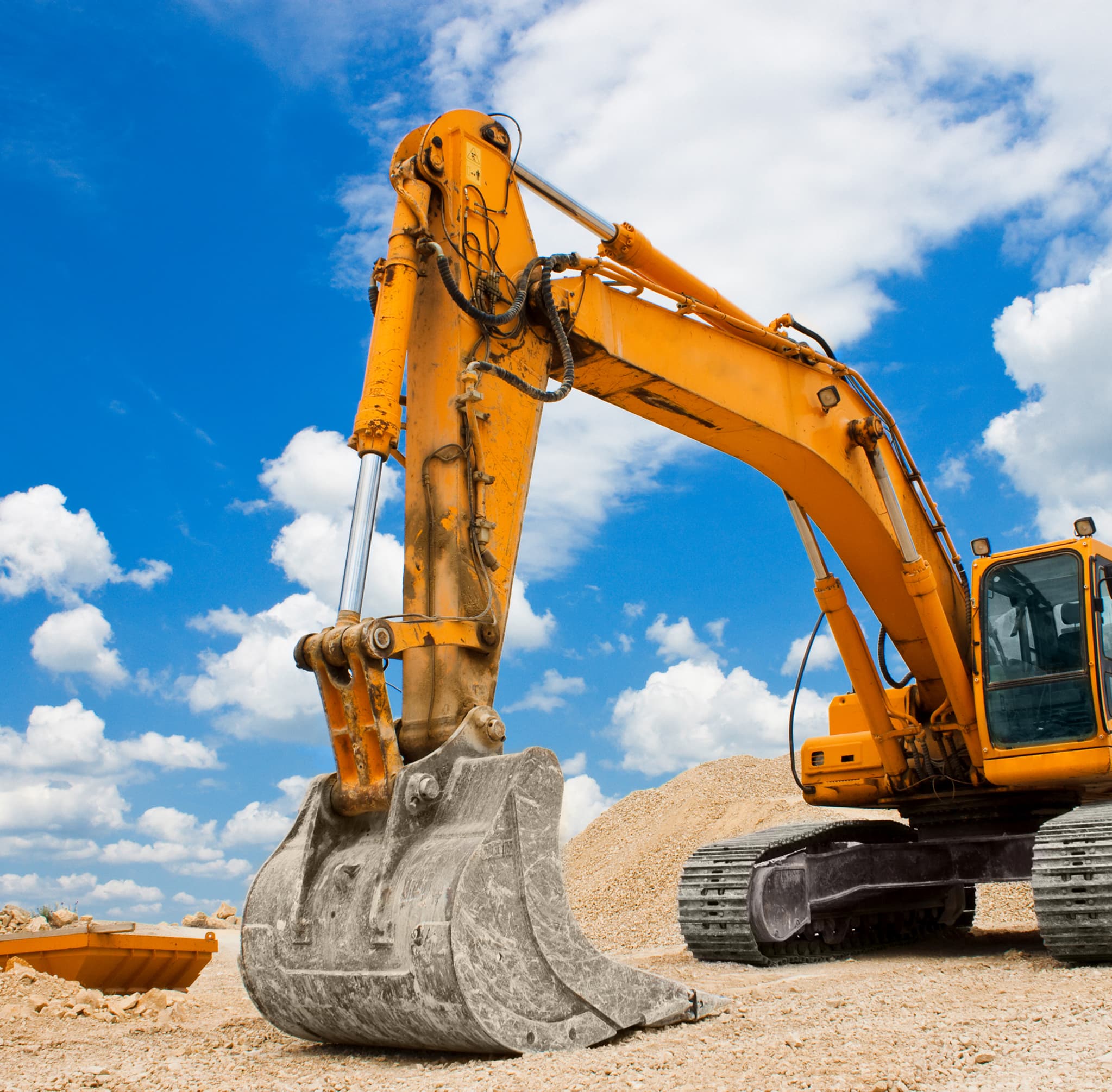 Yellow excavator arm against a blue sky with clouds