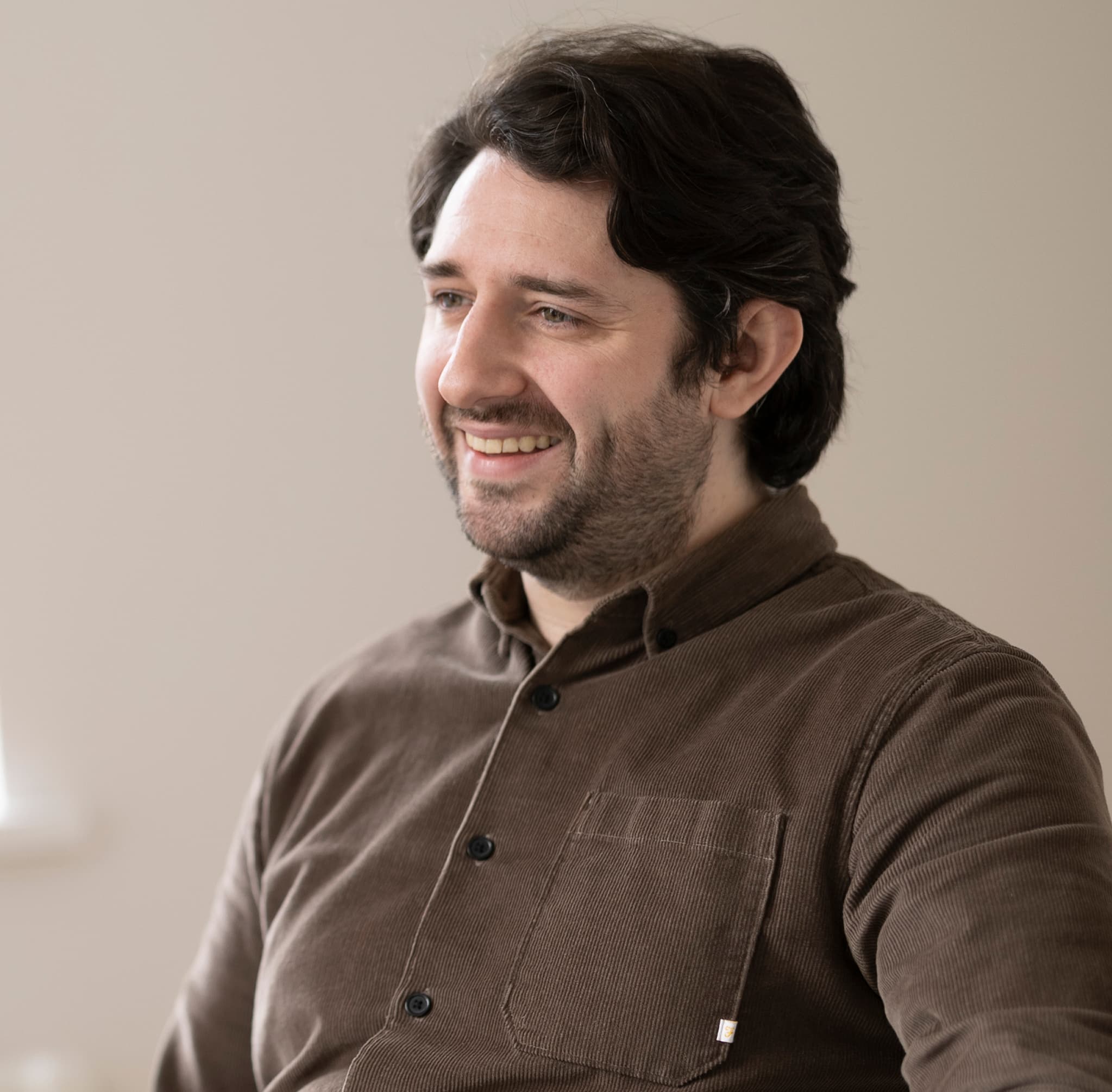 Man with dark hair, smiling, brown/black jacket, indoors